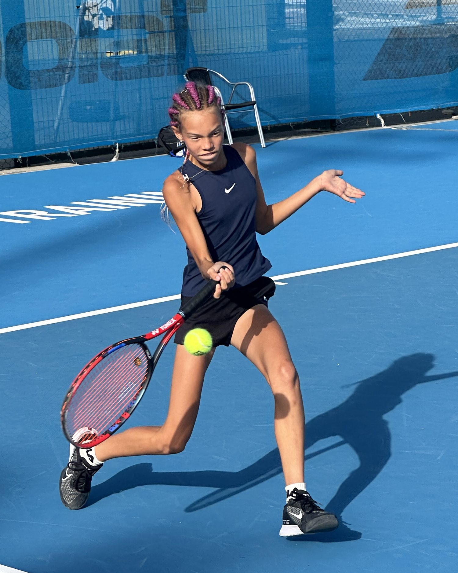 A junior player striking a forehand on the hard courts at T3