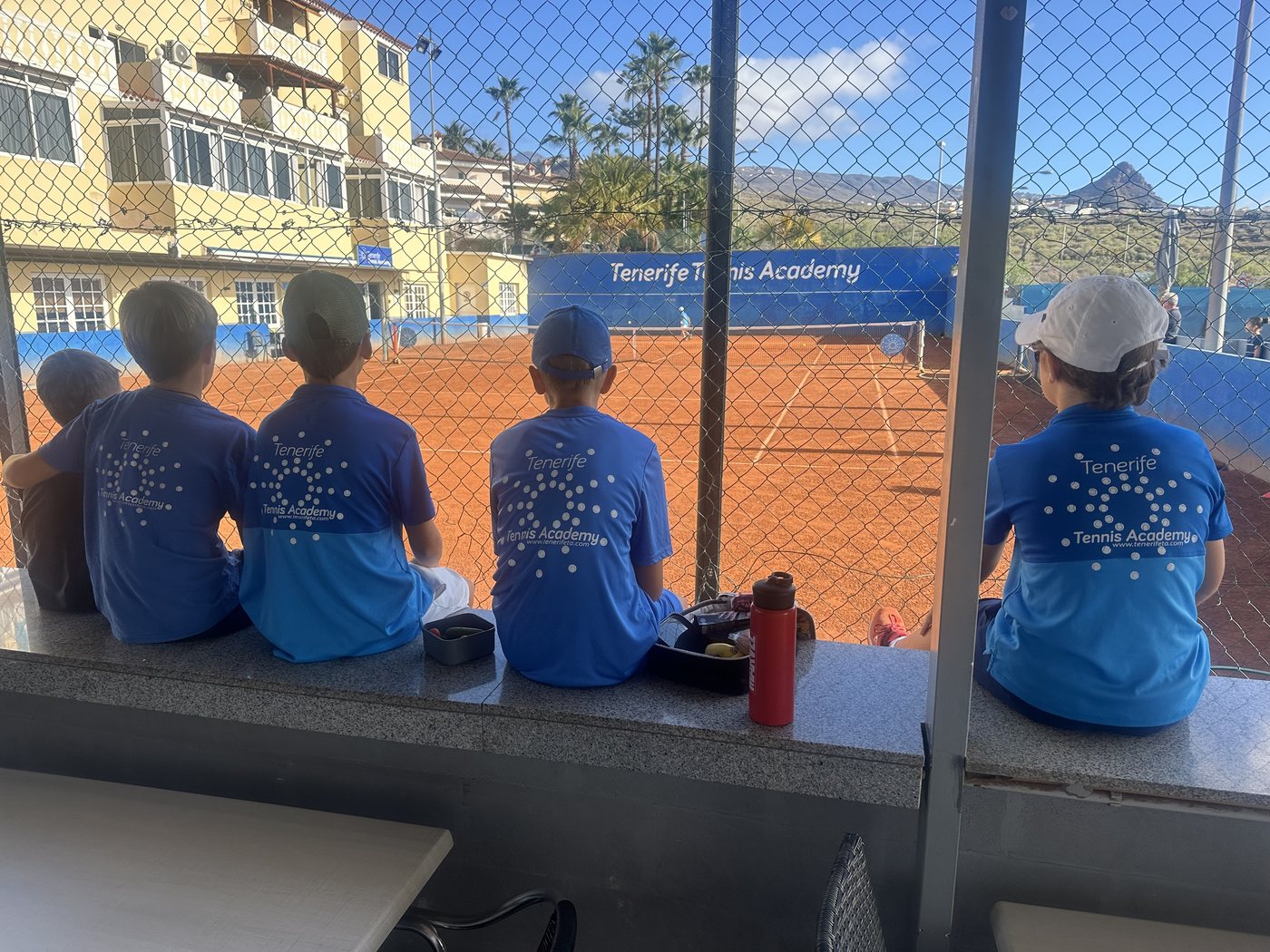 Players in academy kit watching a session courtside at Chayofa