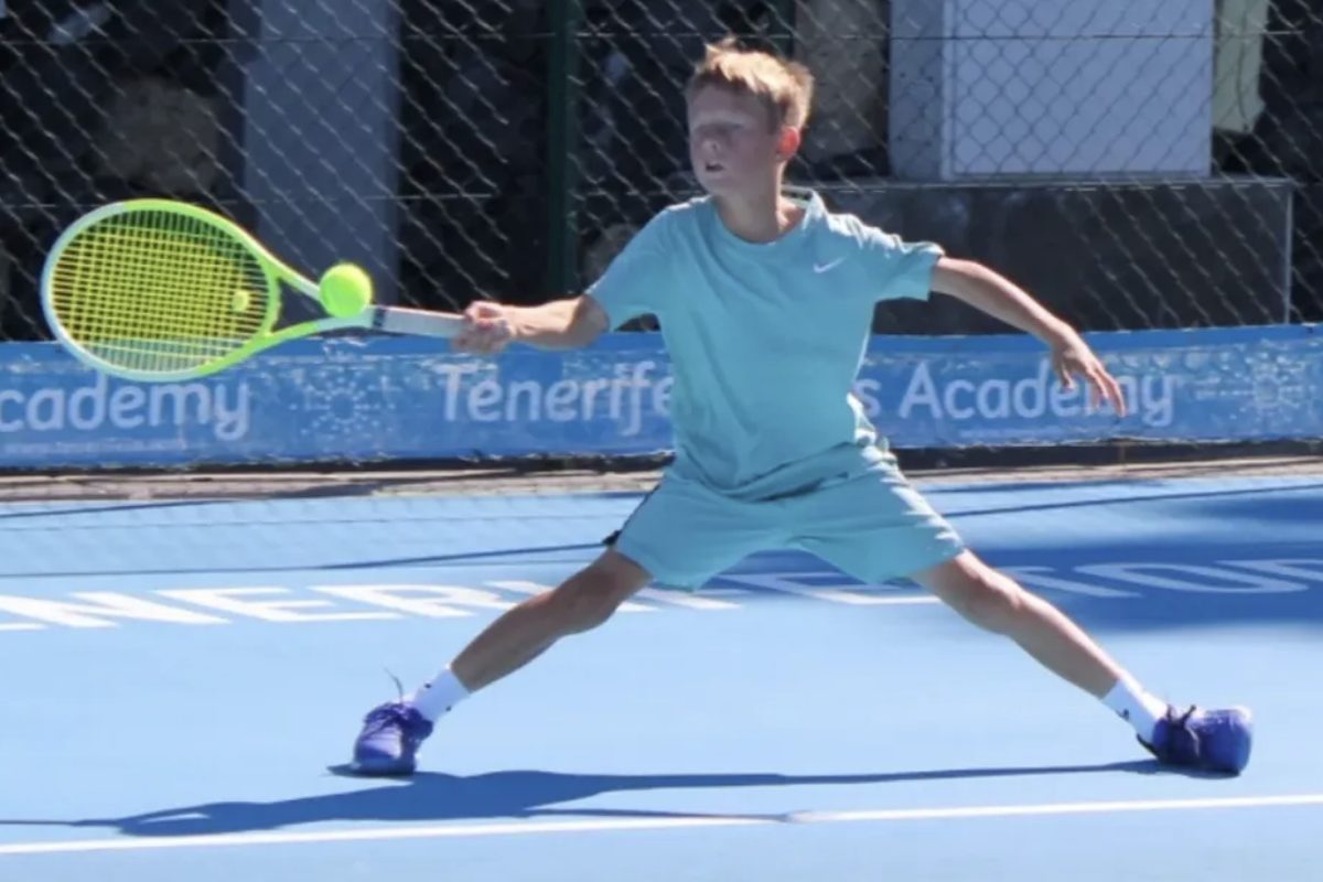 A young player stretching for a forehand on the hard courts in front of the Tenerife Tennis Academy banner
