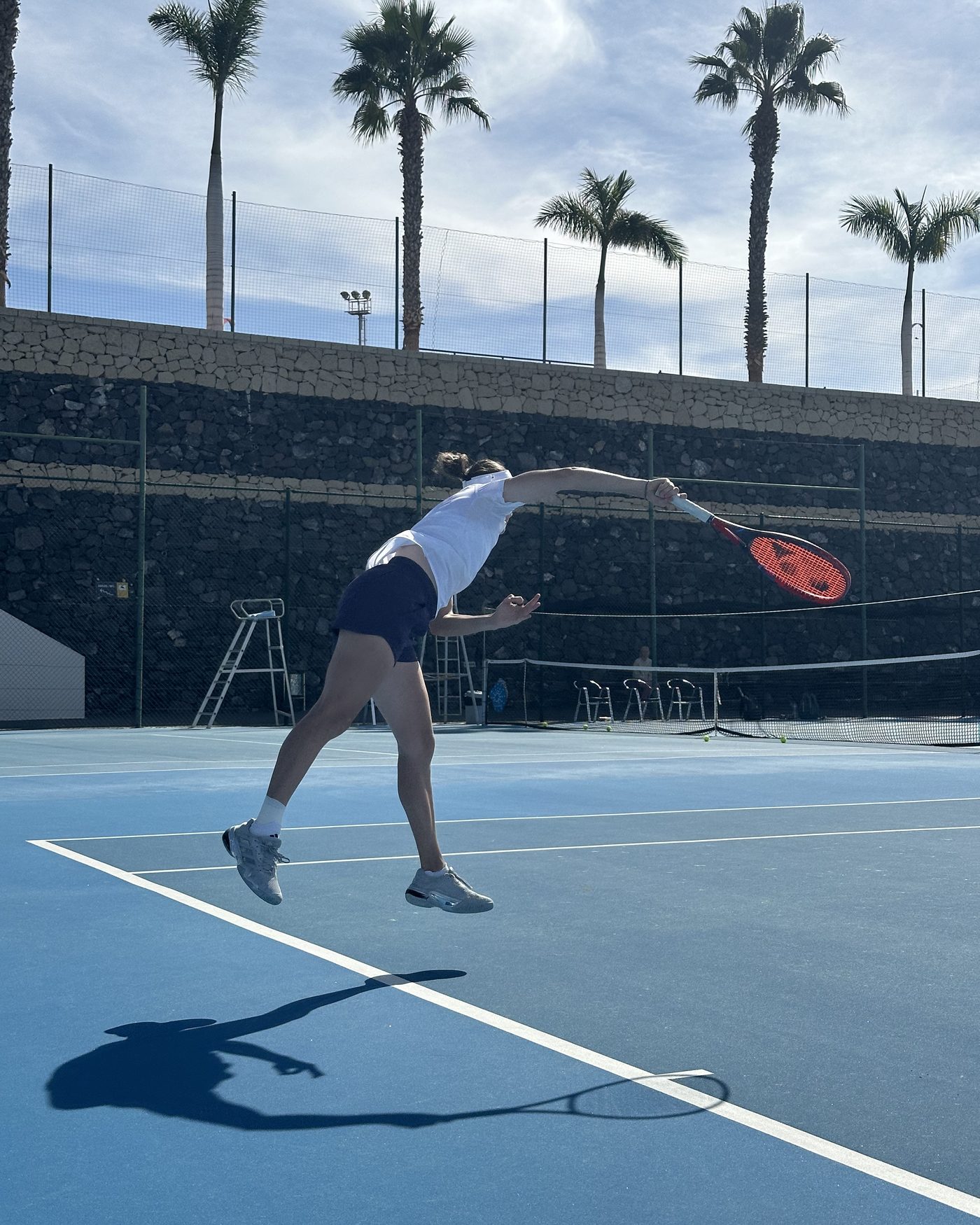A player serving on the hard courts at T3 with palms behind