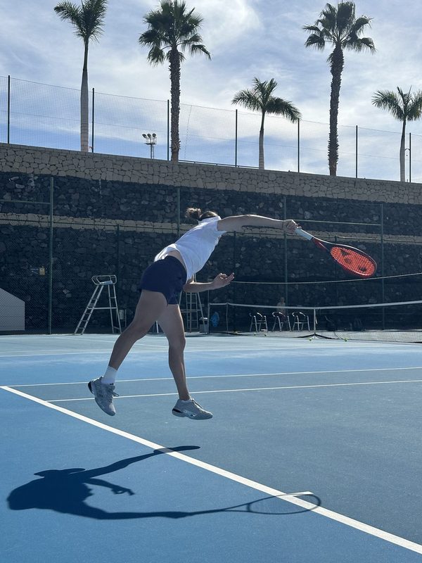 A player serving on the hard courts at T3 with palms behind